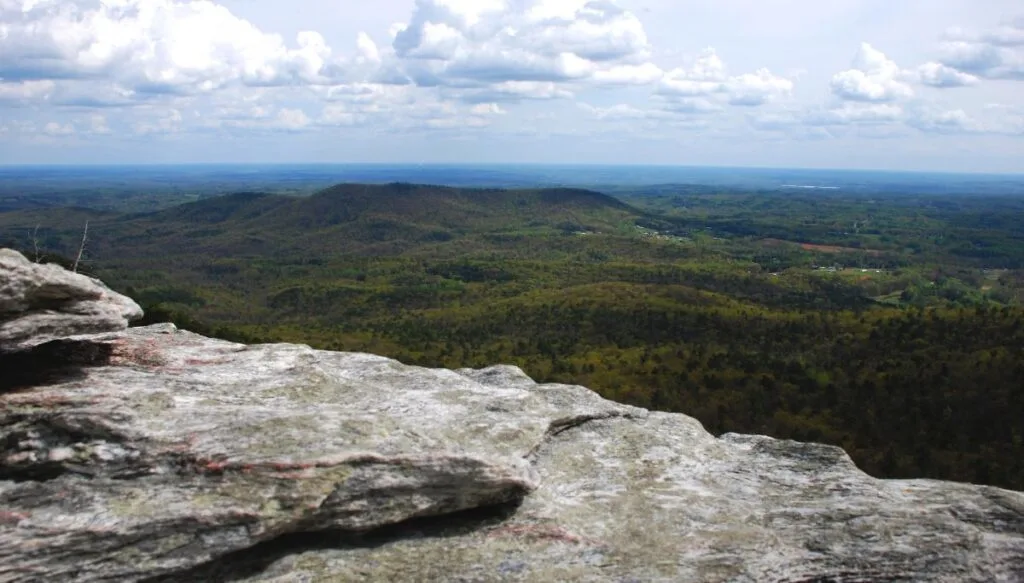 View from the top of Pilot Mountain. You can see vast green forests in the distance and a rock ladge in the foreground. 