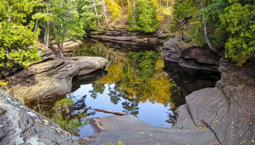 View of a small pool surrounded by large rocks that have pine trees growing on top of them inside Porcupine Mountains Wilderness State Park.