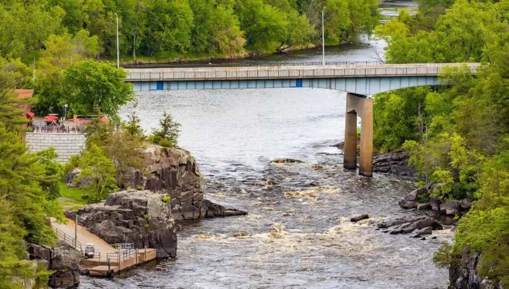 View of a road bridge crossing a river surrounded by green leafy trees along the St. Crois Scenic Byway. 