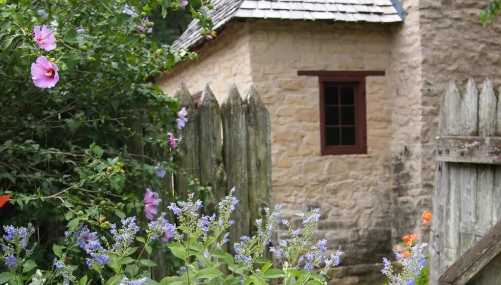 View of an old stone house in Ste. Genevieve with a wooden fance and it is surrounded by flowers in the spring. 