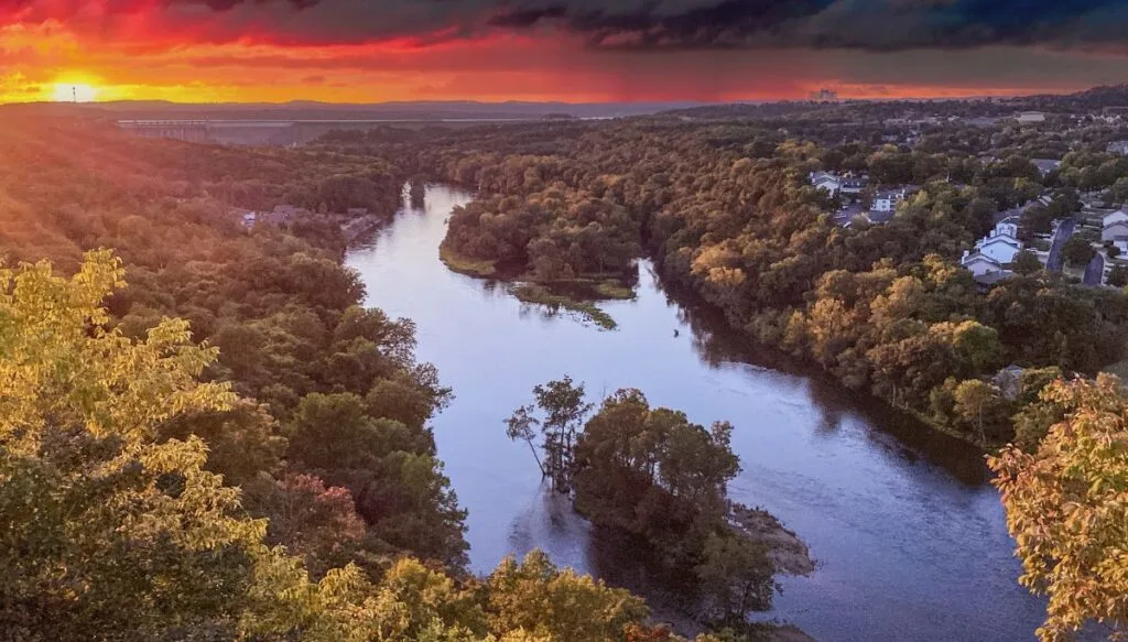 View of the sun setting in the background. You can see Table Rock Lake in the foreground surrounded by green trees. 
