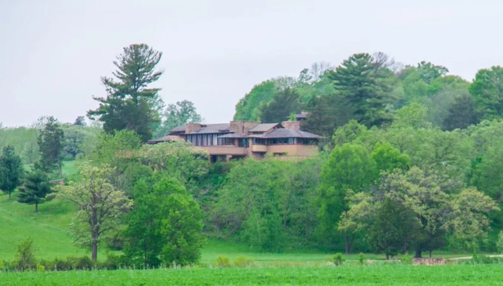 View of a large brown house tucked away in the green forest in Taliesin. 