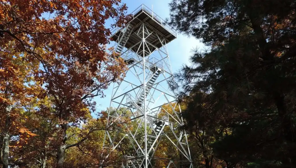 View of a metal fire tower inside of Taum Sauk Mountain State Park. You can see a metal fire tower with metal stairs surrrounded by beautiful fall foliage, 