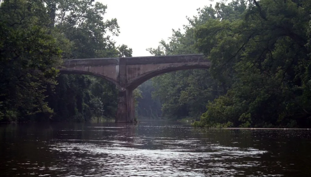 View of Brandywine Creek with an arched bridge over it and surrounded by lots of tall green trees. 
