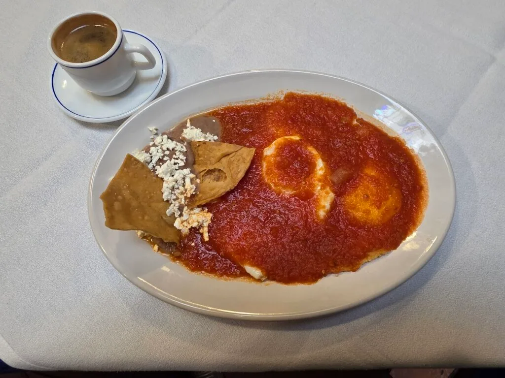 View of eggs in red sauce with beans on the side with cheese and chips. 