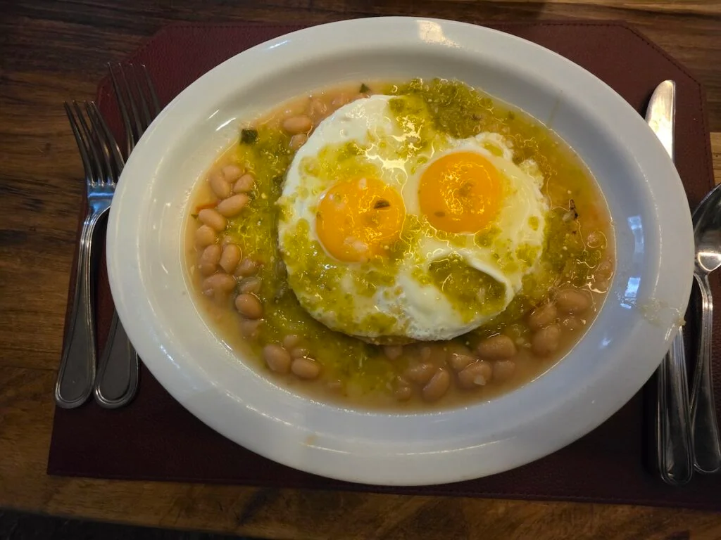 Aerial view of a white plate with two eggs on a bed of white beans and bathed in green sauce. 