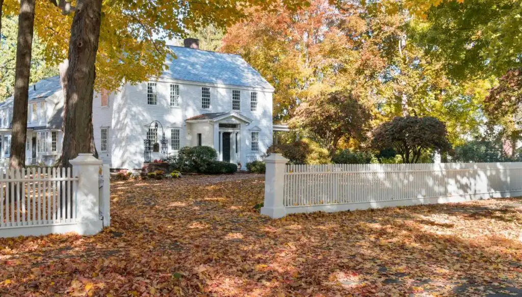 View of a white, Federal-syle home in Deerfields, Massachusetts that is surrounded by vibrant fall foliage. 