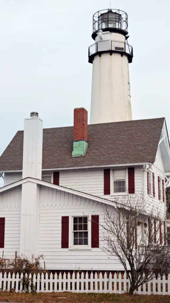 View of the small white lighthouse with a small white house in front of it inside Fenwick Island State Park. 