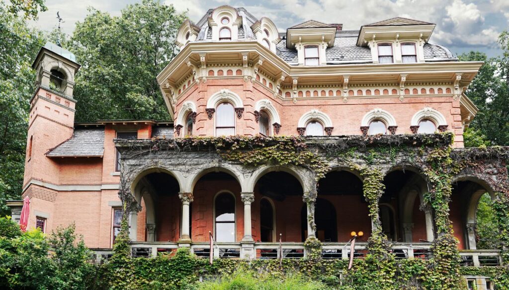 View of the pink Harry Packer mansion in Jim Thorpe. It has Victorian-style architecture with a porch covered in ivy and a tower to the left.