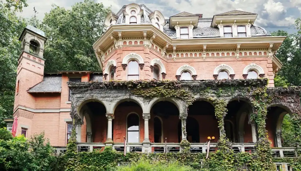 View of the pink Harry Packer mansion in Jim Thorpe. It has Victorian-style architecture with a porch covered in ivy and a tower to the left. 