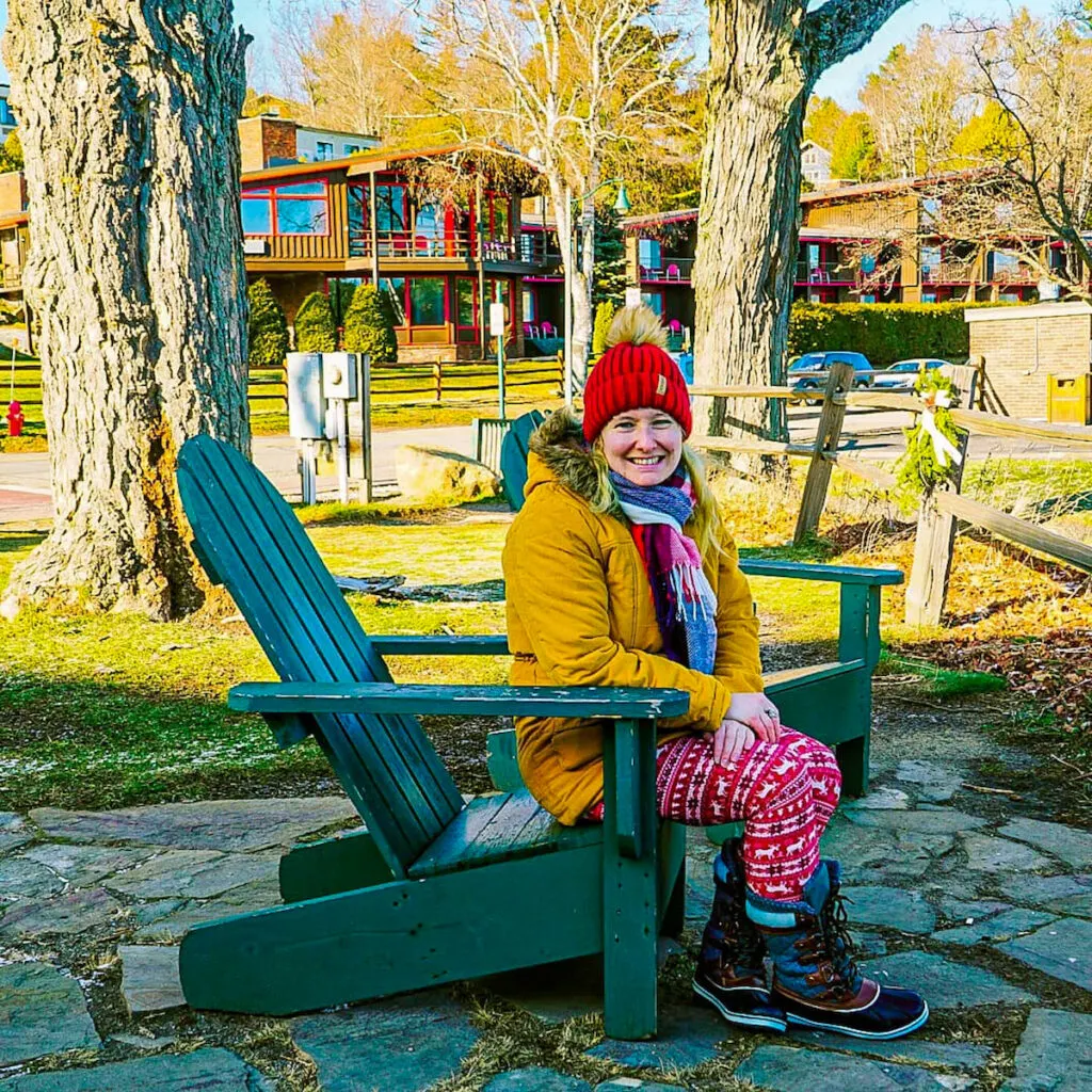 View of me sitting in a green chair in Lake Placid with a yellow coat and a red hat. 