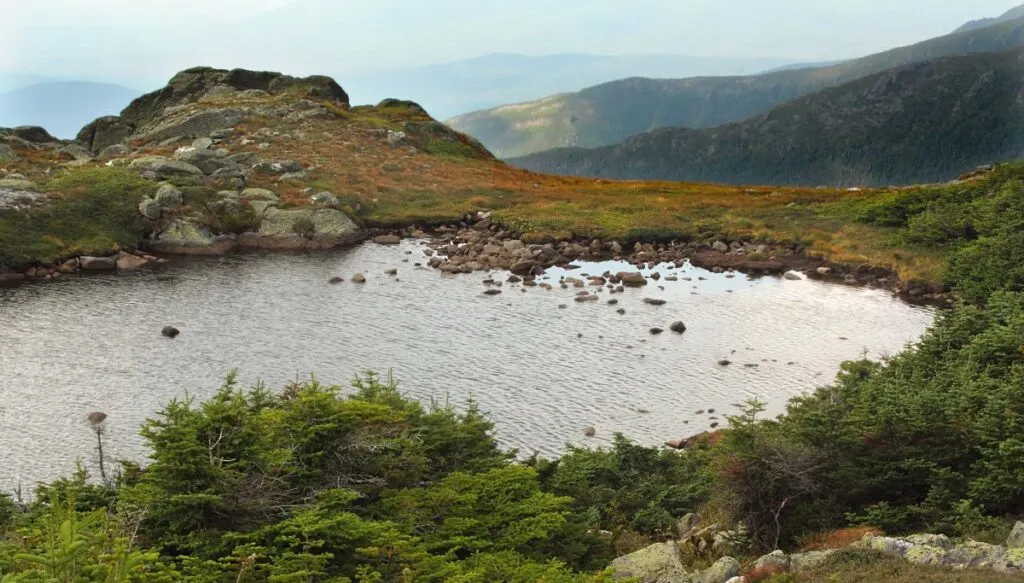 View of a small lake on top of a mountain with short grass all around the edge of the lake. 