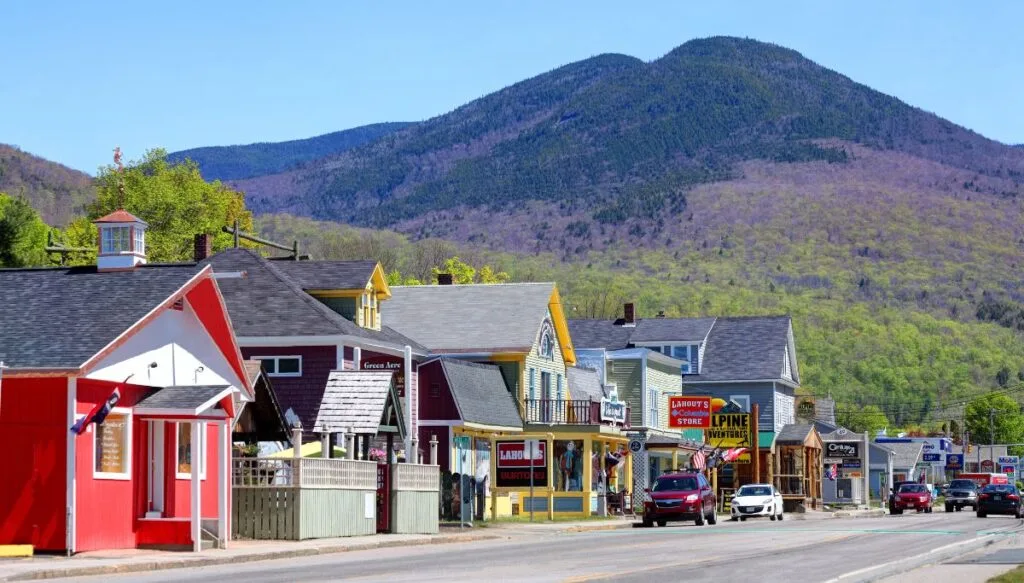 View of the charming little shops and restaurants that line the main street of Lincoln on the left side of the main road. You can also see a giant green mountains in the background on a sunny day. 