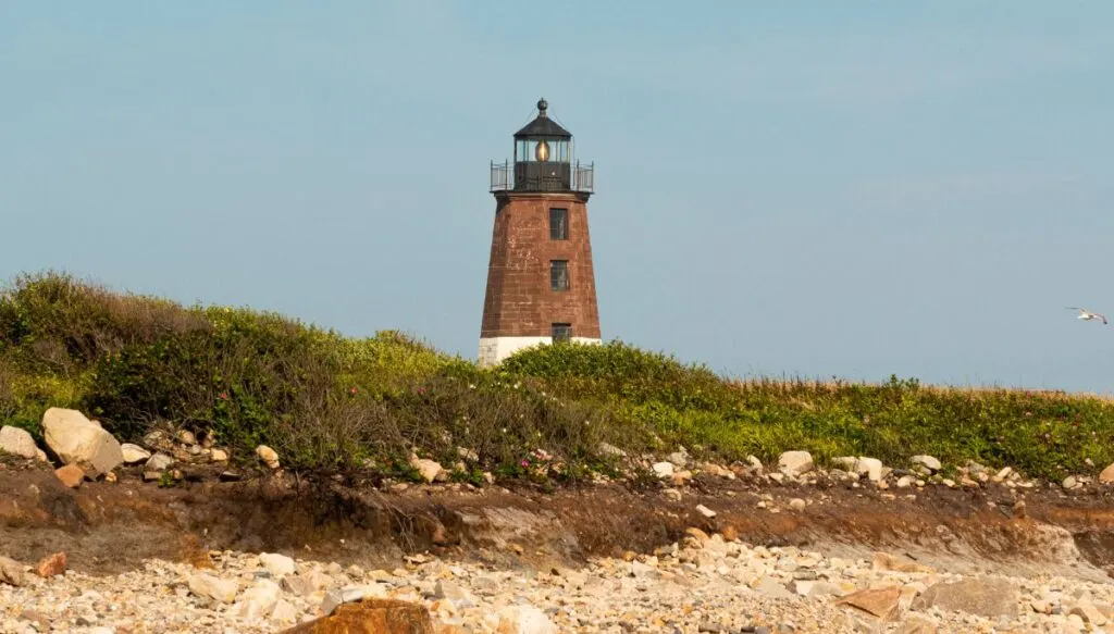 View of a small brick lighthouse poking up through green grass in Narragansett. 