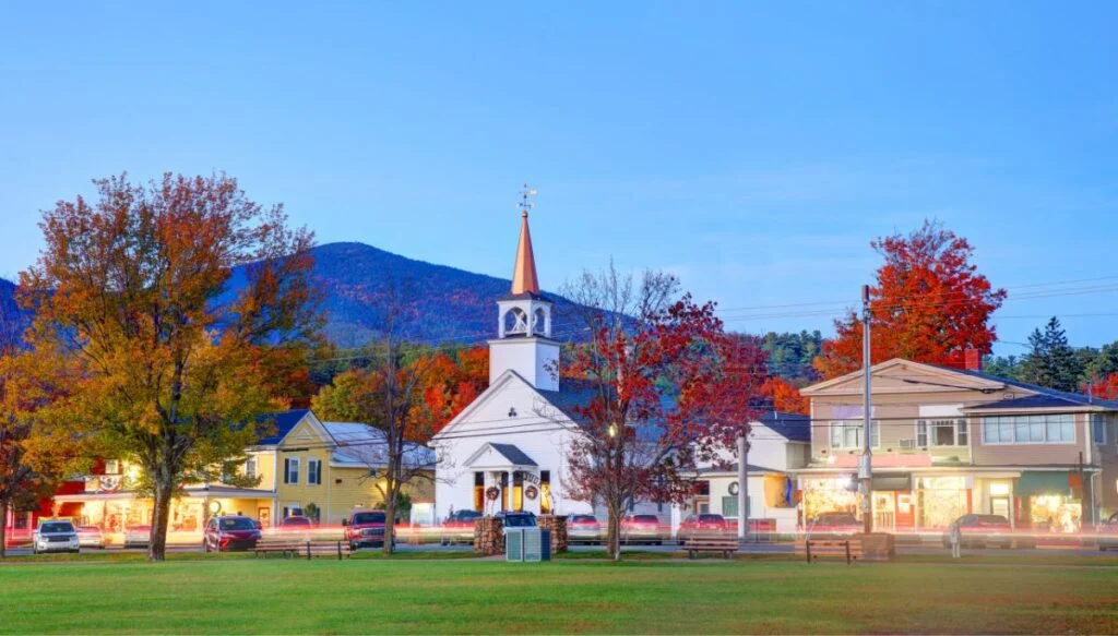 View of a white steepled church sitting along a main road surrounded by vibrant fall foliage in North Conway, New Hampshire. 