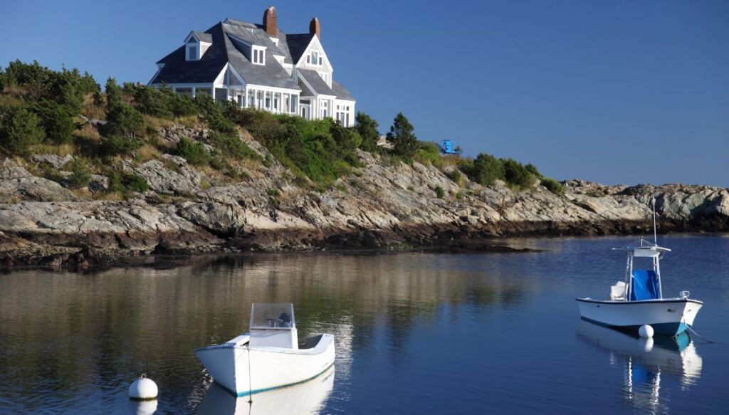 View of boats bobbing in the water with a large white house on a cliff in the background along Ocean Drive.