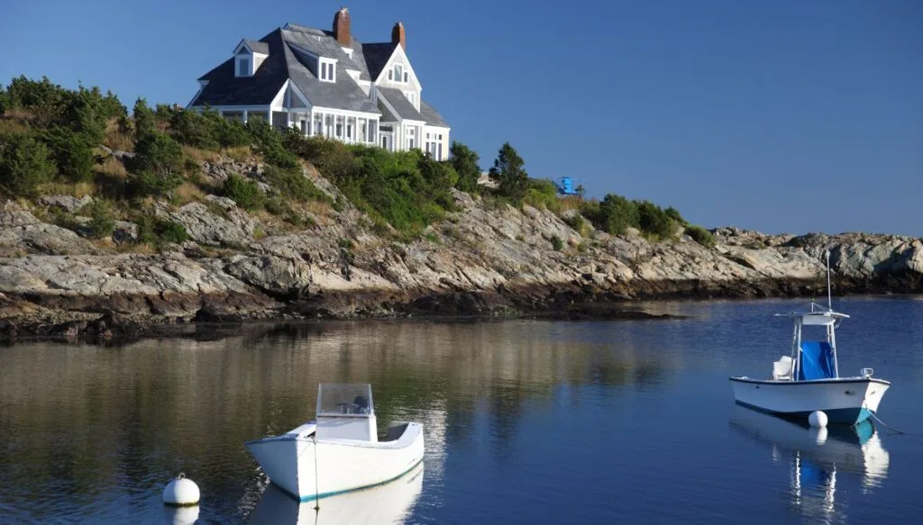 View of boats bobbing in the water with a large white house on a cliff in the background along Ocean Drive. 