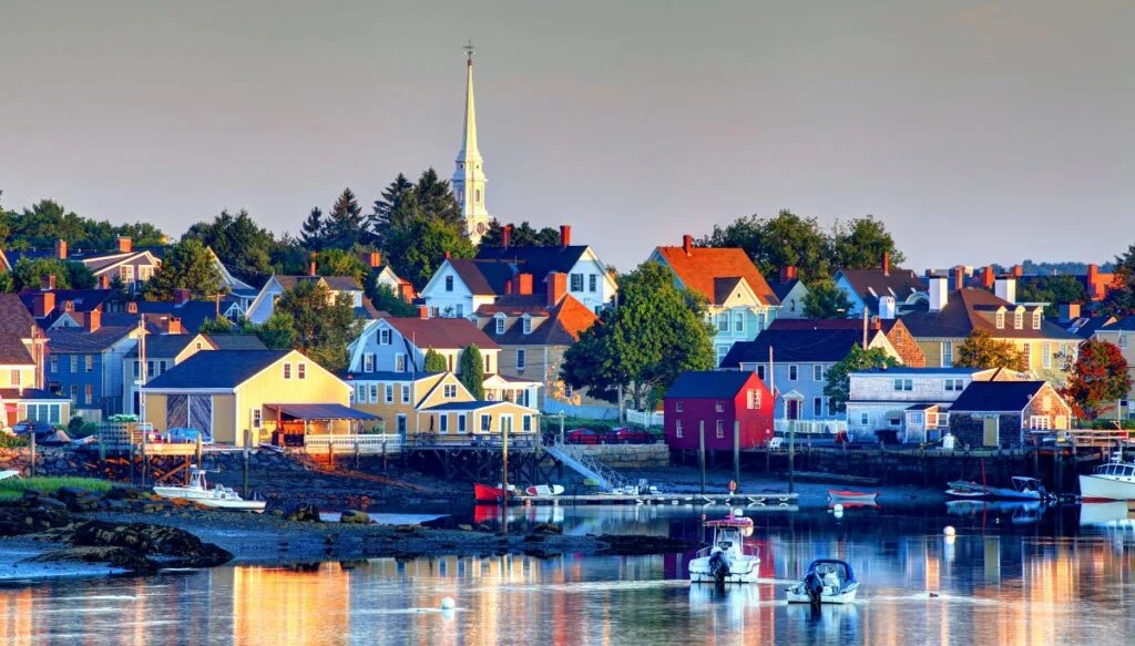 View of colorful homes sitting along the weter with boats in the foreground and a white steeple in the background at Portsmouth. This is one of the most beautiful places in New Hampshire. 