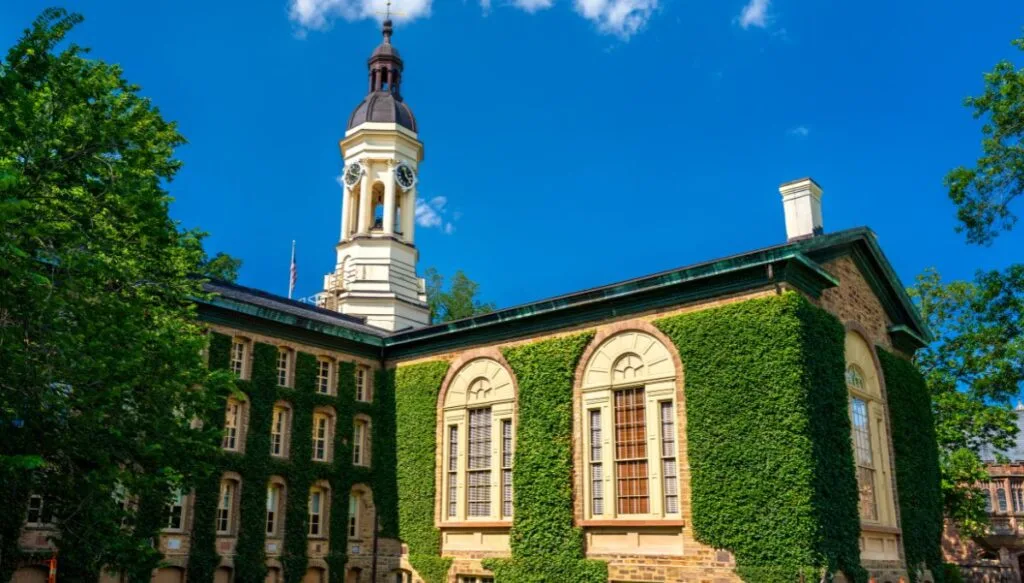 View of Nassau Hall in Princeton covered in ivy with a steeple on top on a sunny day. 