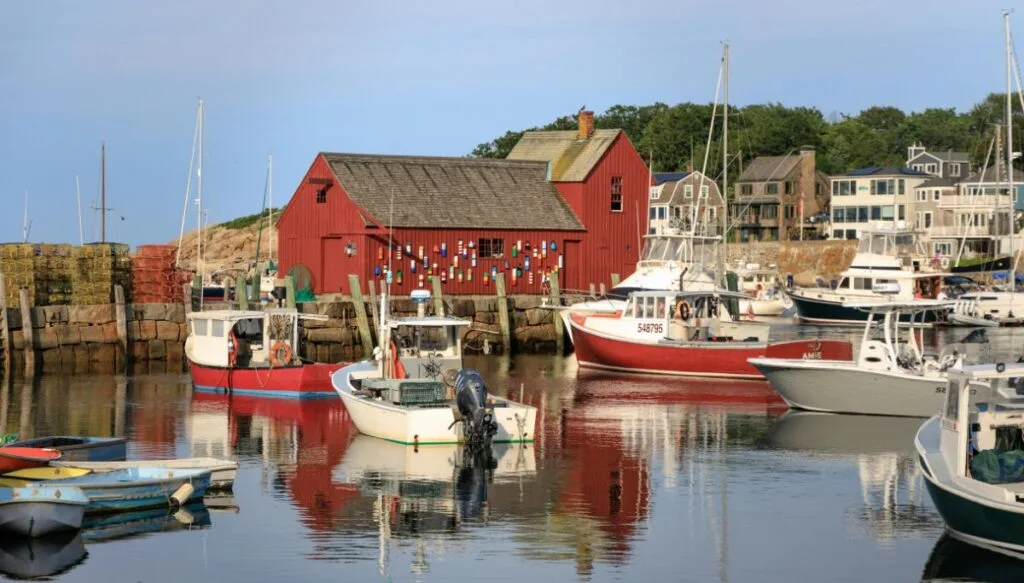 View of lobster boats in the harbor in Rockport with a red building in the background with a ton of lobster buoys on it. 