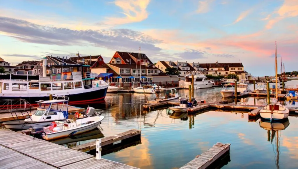 View of the harbor in Salem, Massachusetts. You can see the sky turning pink and buildings along the water with boats in the water. 