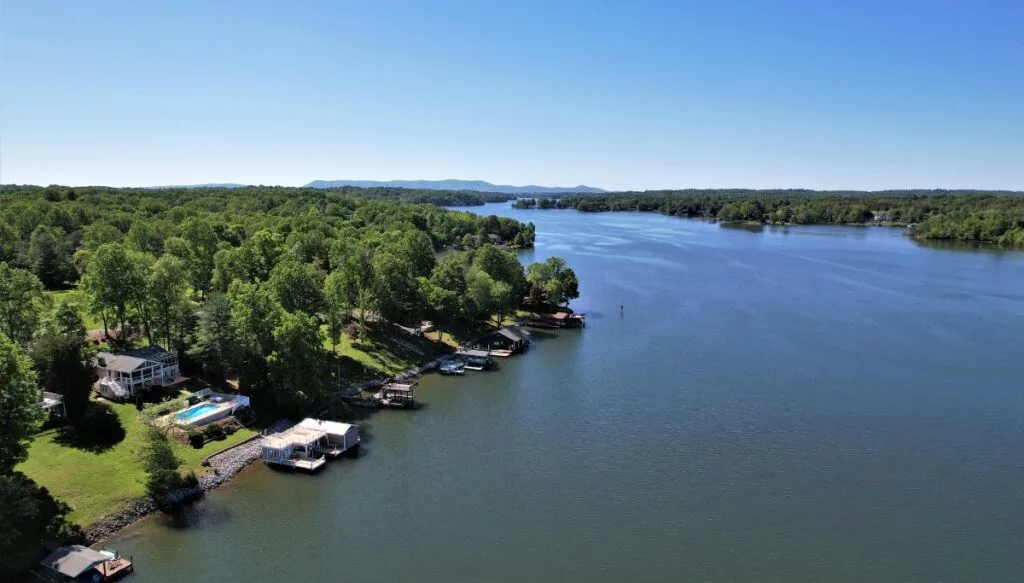 Aerial view of Smith Mountain Lake with houses on the edge of the lake and green trees in the back and off in the distance on a sunny day. 