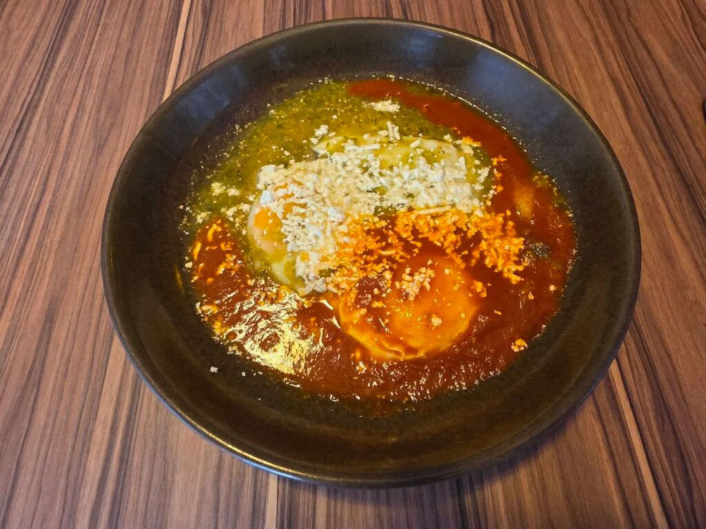 Aerial view of Huevos Divorciados with green and red sauce in a black bowl on a wooden table in Tezontle Restaurant. 