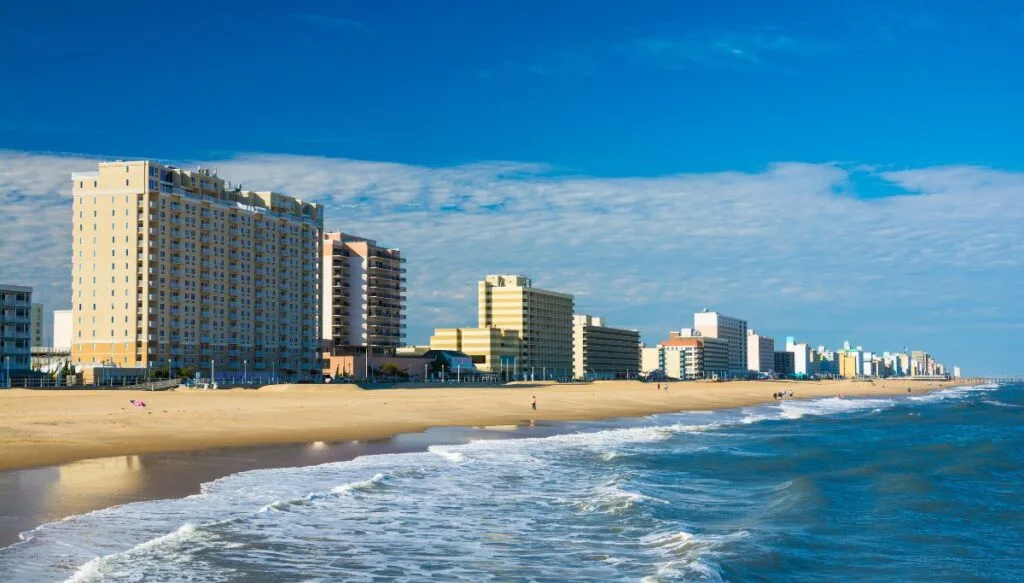 View of Virginia Beach with the sand in the front of large buildings ad the the wave from the ocean rolling in on a sunny day. 