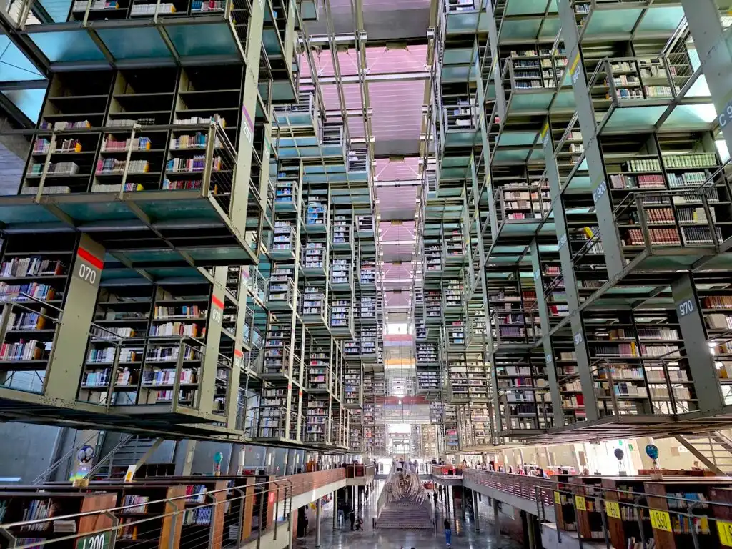 View of the interior of Biblioteca Vasconcelos with bookshelves that look like they almost float in the air, with lots of light that comes in through the windows. 
