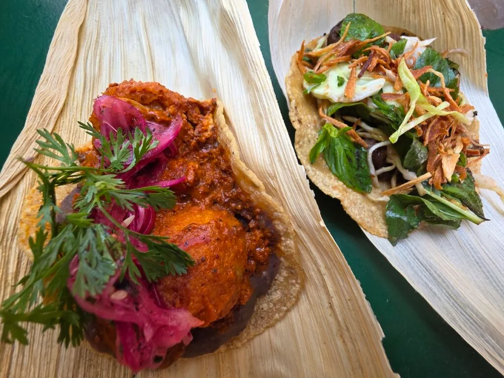 Aerial view of two vegetarian tacos sitting on old corn husks and piled high with fresh herbs. This is one of the best restaurants in Mexico City. 