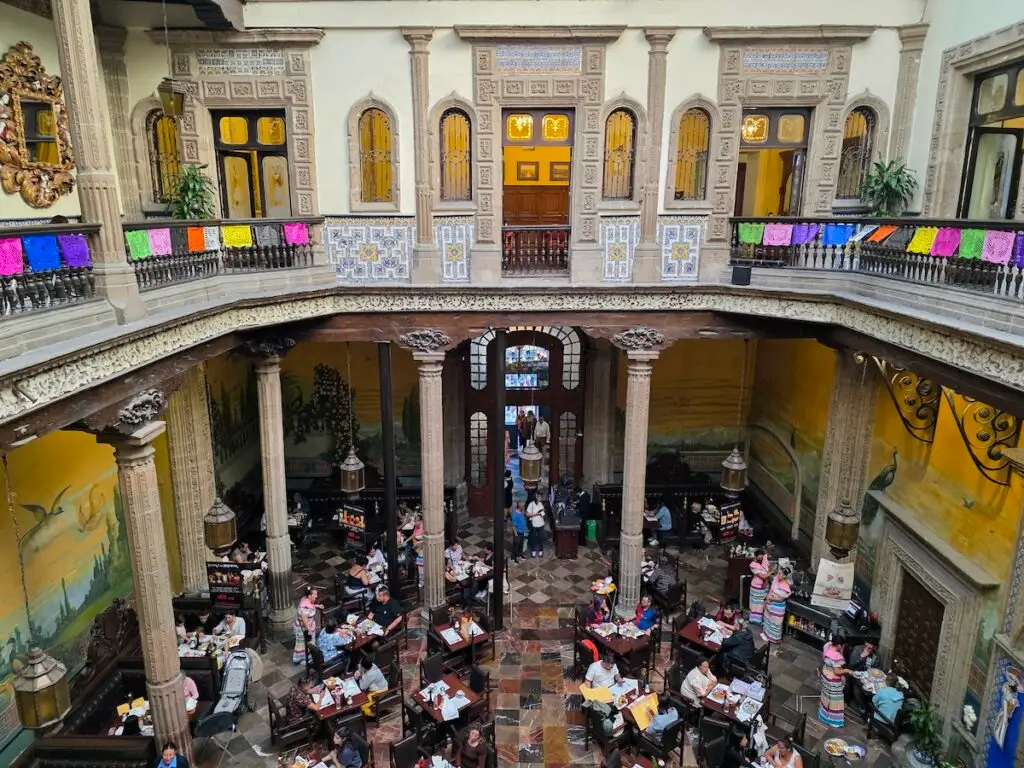View of the central courtyard with peoplewating at atbles inside of Casa de Los Azulejos. 