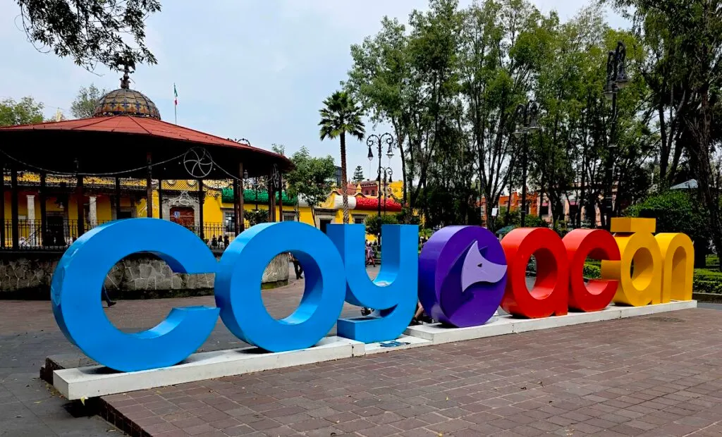View of an outdoor plaza in Coyoac&aacute;n with a sign that says, "Coyoac&aacute;n" in blue, purple, red, and yellow letters. 