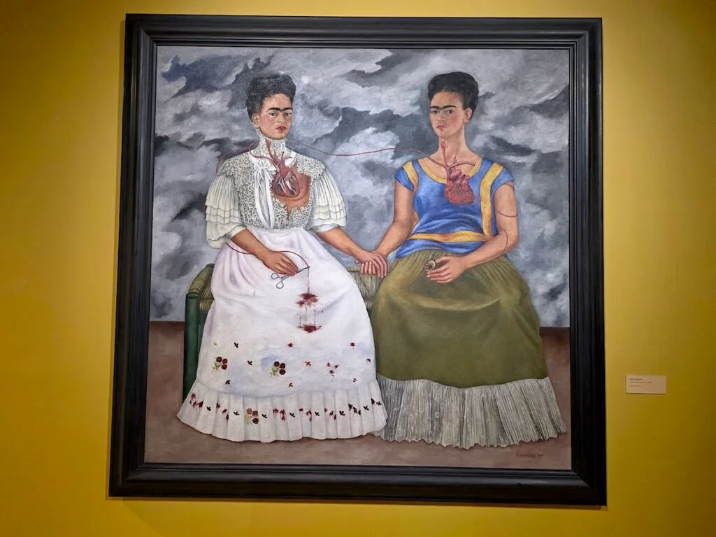 View of a painting of the Two Fridas sitting on a yellow wall inside the Museo de Arte Moderno. A visit to this museum is easily one of the best free things to do in Mexico City. 