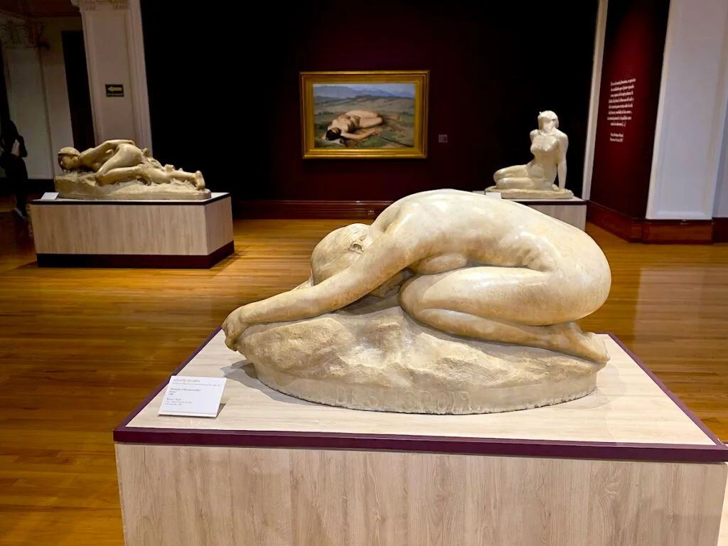 View of three marble statues inside MUNAL with a painting in the background. 