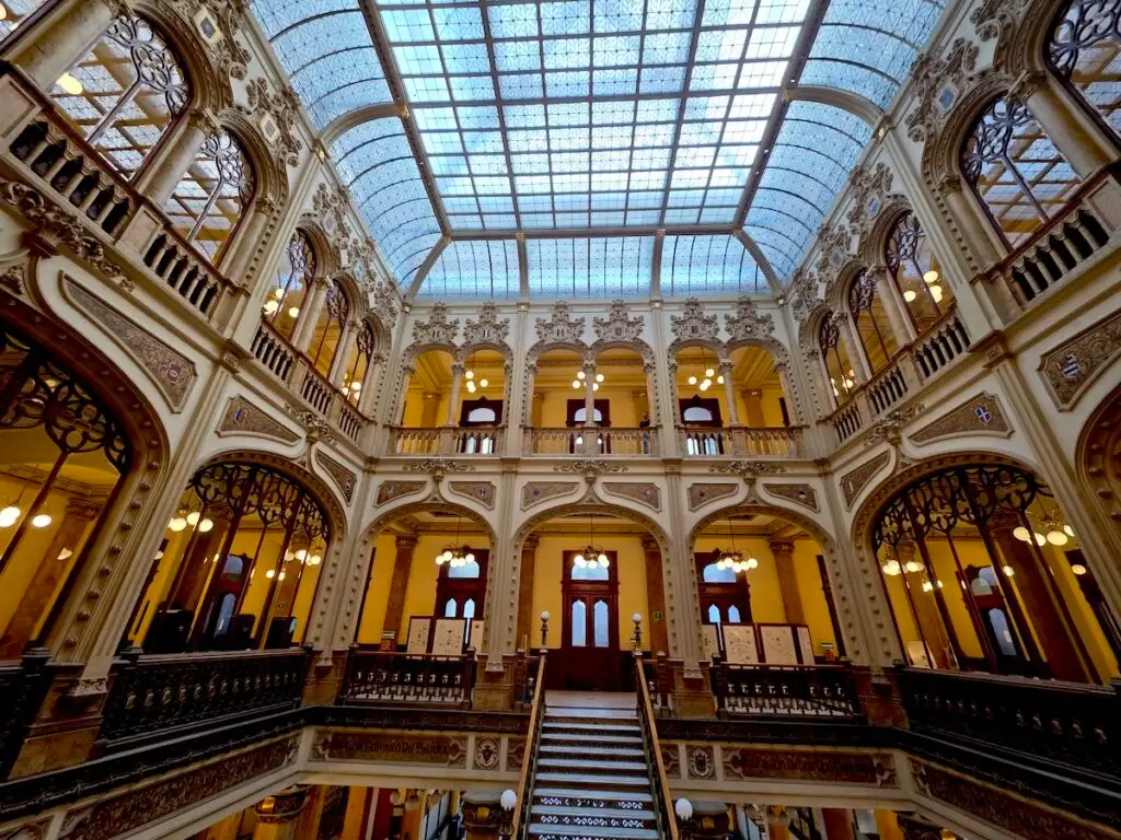 View of the orante interior of the Palacio Postal. You can see arched floors with yellow walls and a glass roof at the top.