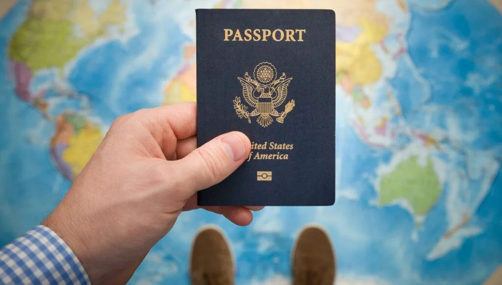 View of a man holding an American passport over a world map. 