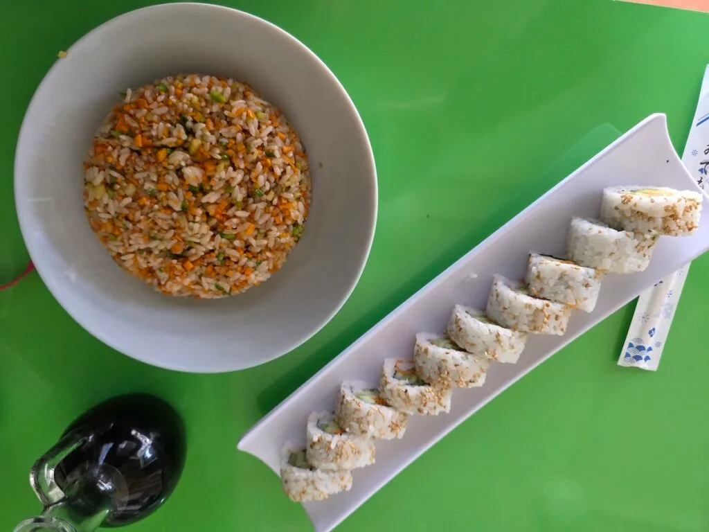 Aerial view of a bowl fo rice and a veggie roll on top of a green table at Sushi Kona. 