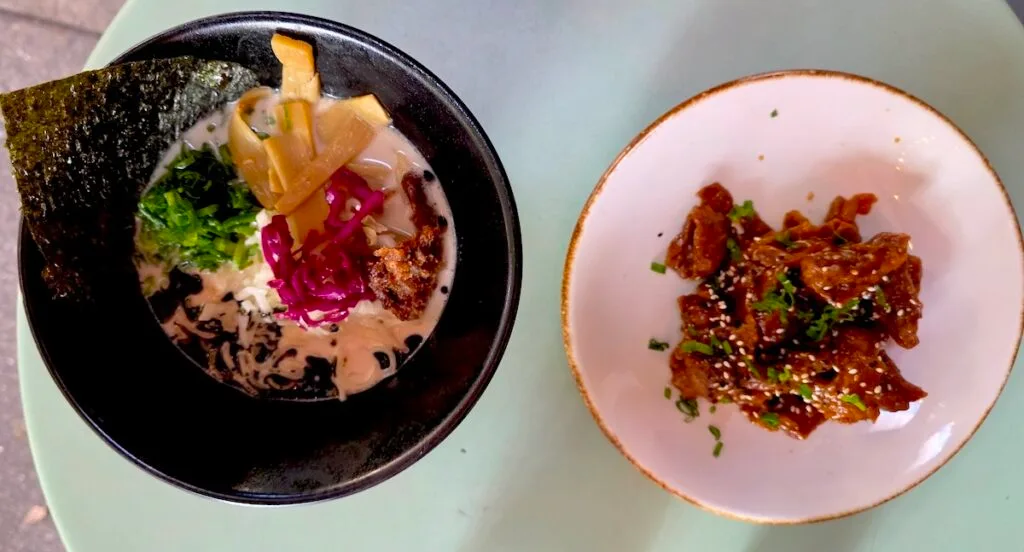 Aerial view of a bowl of vegan ramen on the left and a plate of orange chicken on the right from Vegan Ramen Mei. 