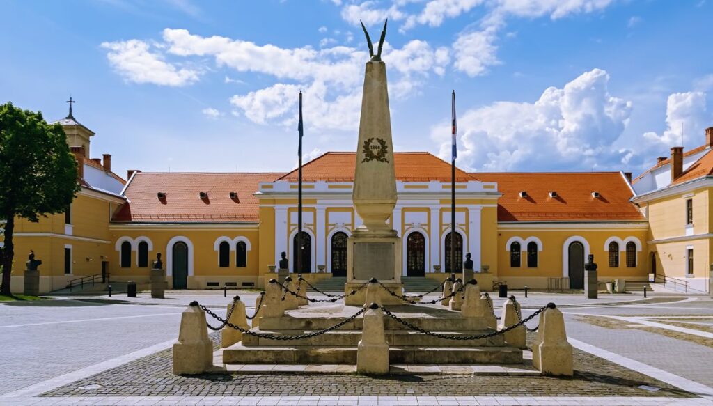 A view of Alba Carolina Citadel with a stone statue in the foreground and a yellow building behind it in a courtyard.