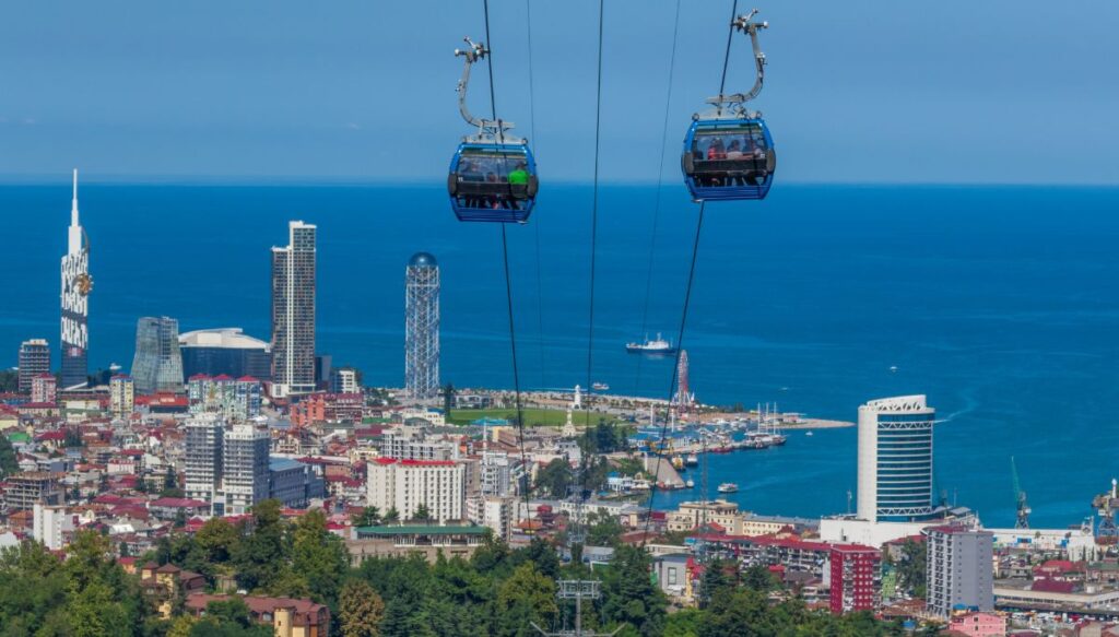 View of blue cable cars going up and down the mountain with a view of Batumi along the coast at the bottom of the photo. 