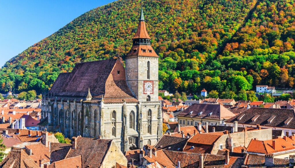 View of the church in Brasov surrounded by red roofed buildings and trees changing colors in the background. This is one of the most beautiful places in Romania.