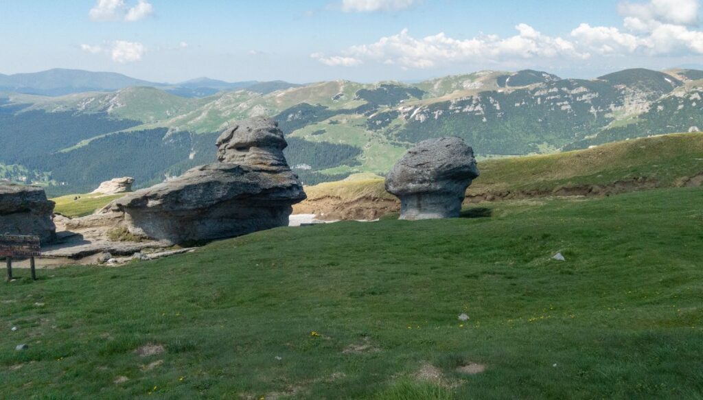 View of unique rock formations in Bucegi National Park with beautiful green mountains in the background.