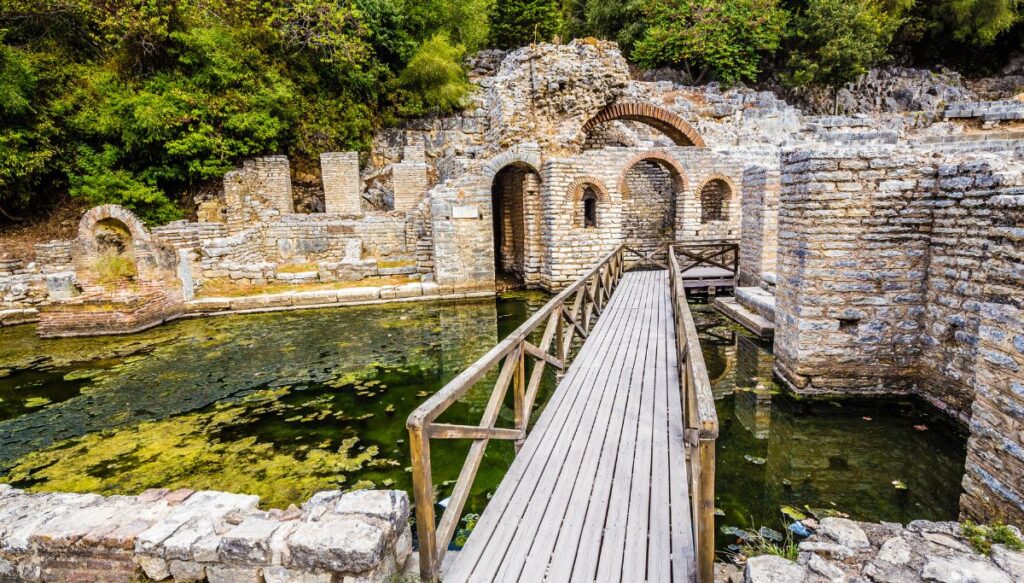 View of ancient stone buildings sitting in water with a walkway leading to them in Butrint National Park.