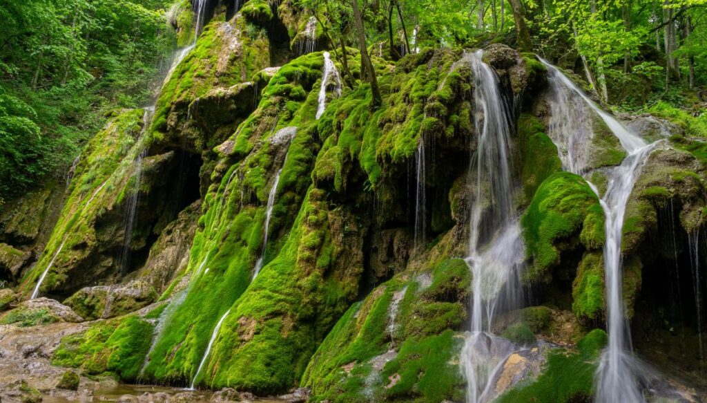 View of tiny waterfalls spilling over moss covered rocks inside of Cheile Nerei in Romania.