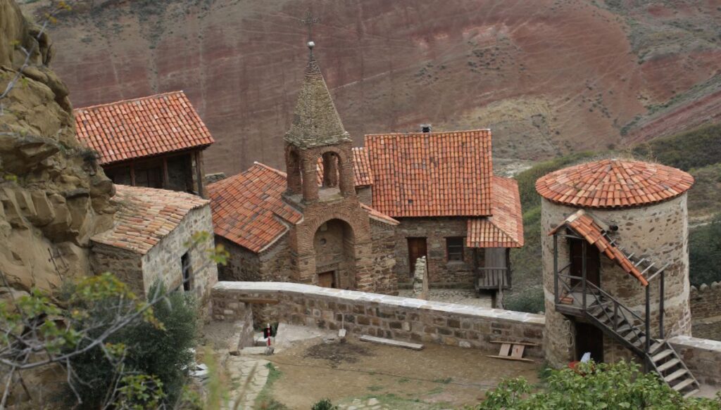 View of the red roofed stone buildings along the edge of David Gareja Monastery and overlooking the surrounding mountains. 