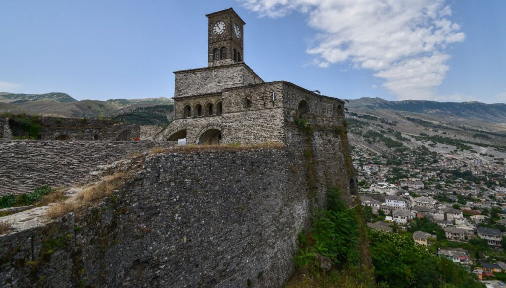 View of a stone castle with a clock tower on it with the mountains all around in Gjirokastër.