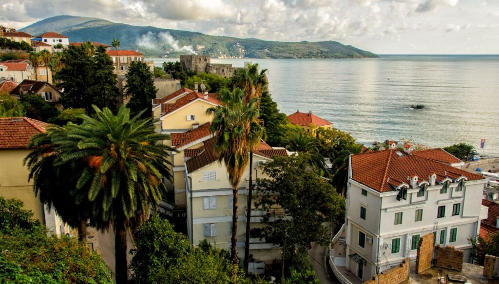 View of several Colonial-style homes sitting alone the coast in Herceg Novi. You can see the water in the distance and lots of palm trees in one of the most beautiful places in Montenegro. 