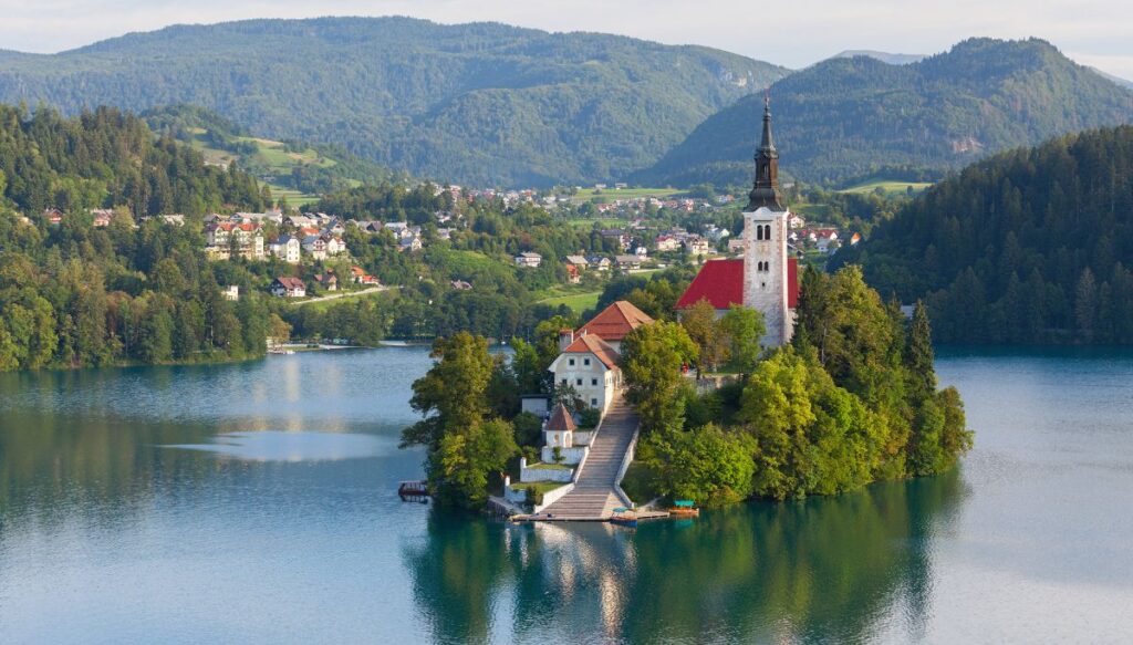 View of a long set of stairs leading up to a church with a steeple on a small island in the middle of Lake Bled.