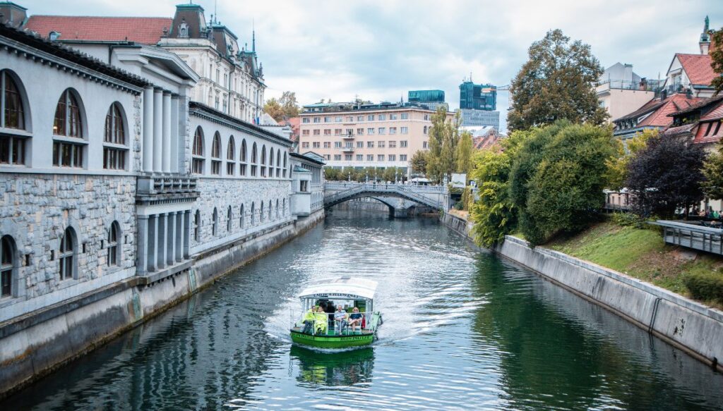 View of a green boat sailing through the river in Ljubljana, one of the most beautiful places in Slovenia.