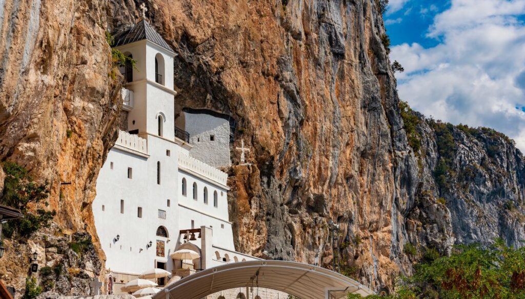 View of the white Ostrog Monastery built into the side of a mountain in Montenegro. 
